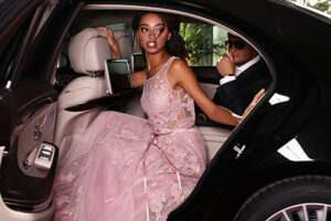 fashion photo of gorgeous mulatto woman with long dark hair wears luxurious dress and man in elegant costume,arrived on red carpet event in black car